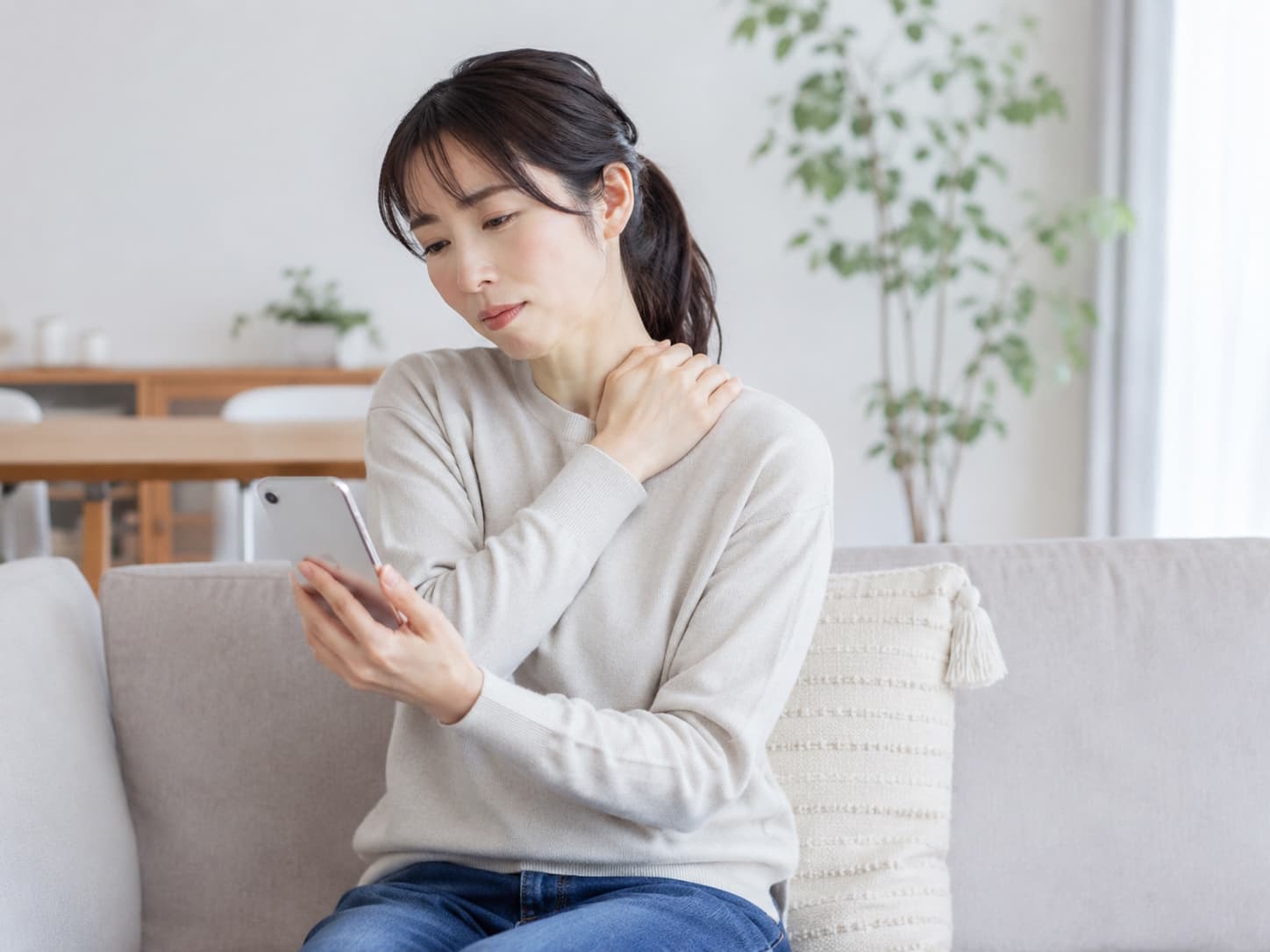 ソファに座り、首に手を当てて不調を気にしている女性